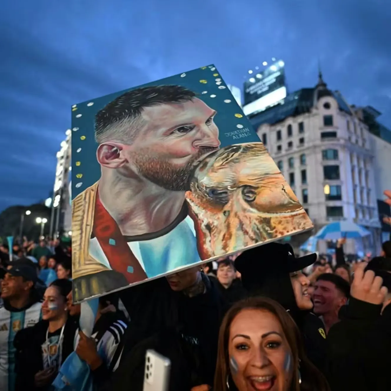 Une supportrice de l'Argentine brandit une pancarte repr&eacute;sentant la star du football argentin Lionel Messi embrassant le troph&eacute;e de la Coupe du monde, apr&egrave;s la demi-finale de la Coupe du monde de football 2026, au pied de l'Ob&eacute;lisque de Buenos Aires, le 15 juillet 2026. (LUIS ROBAYO / AFP)